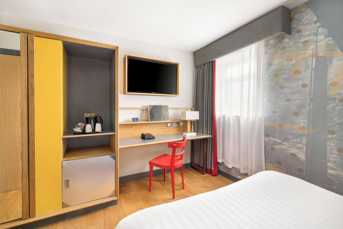 Una habitación de hotel con cama, escritorio con silla, televisión y armario.