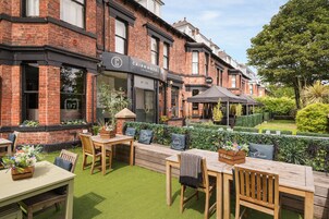 A hotel with outdoor seating, a brick facade, and a well-maintained garden.