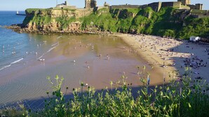 Ein Strand mit einer historischen Burg auf einem Felsen mit Blick aufs Meer.