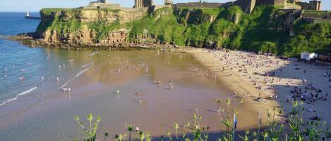 Una playa con un castillo histórico en un acantilado con vistas al mar.