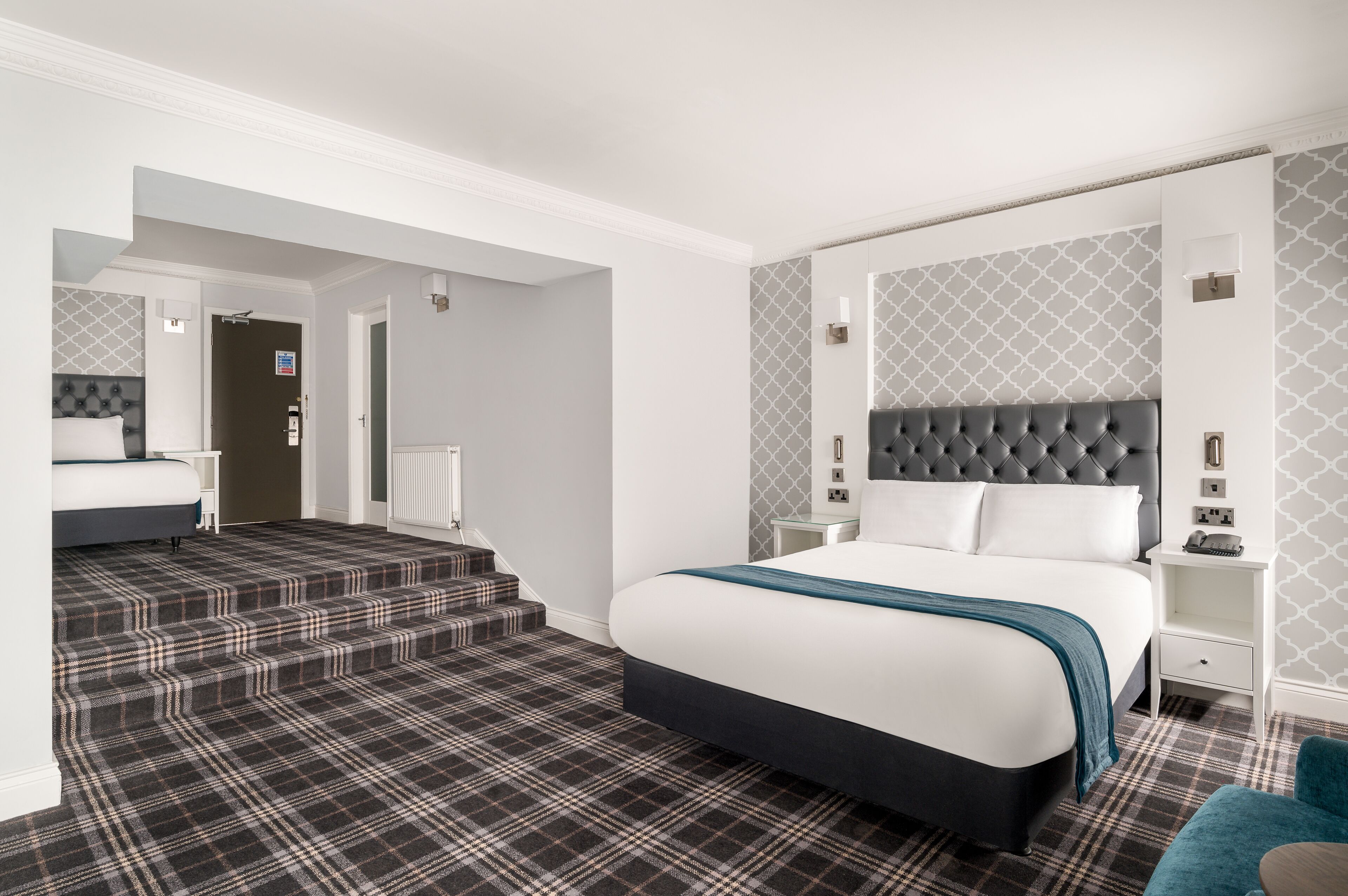 Une chambre d’hôtel moderne avec un grand lit, une tête de lit, une table de chevet et un escalier recouvert de moquette.