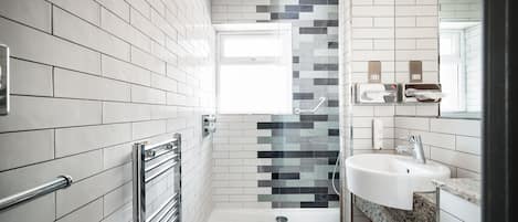 Ein modernes Badezimmer mit weißen Fliesen, einer Glasdusche, einem weißen Waschbecken und einem Waschtisch mit Granitplatte.