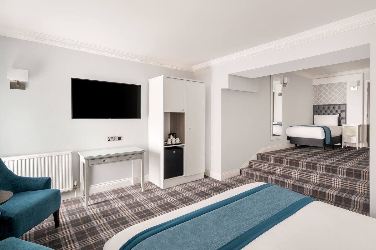 Una habitación de hotel con cama, escritorio, silla, televisor y armario.