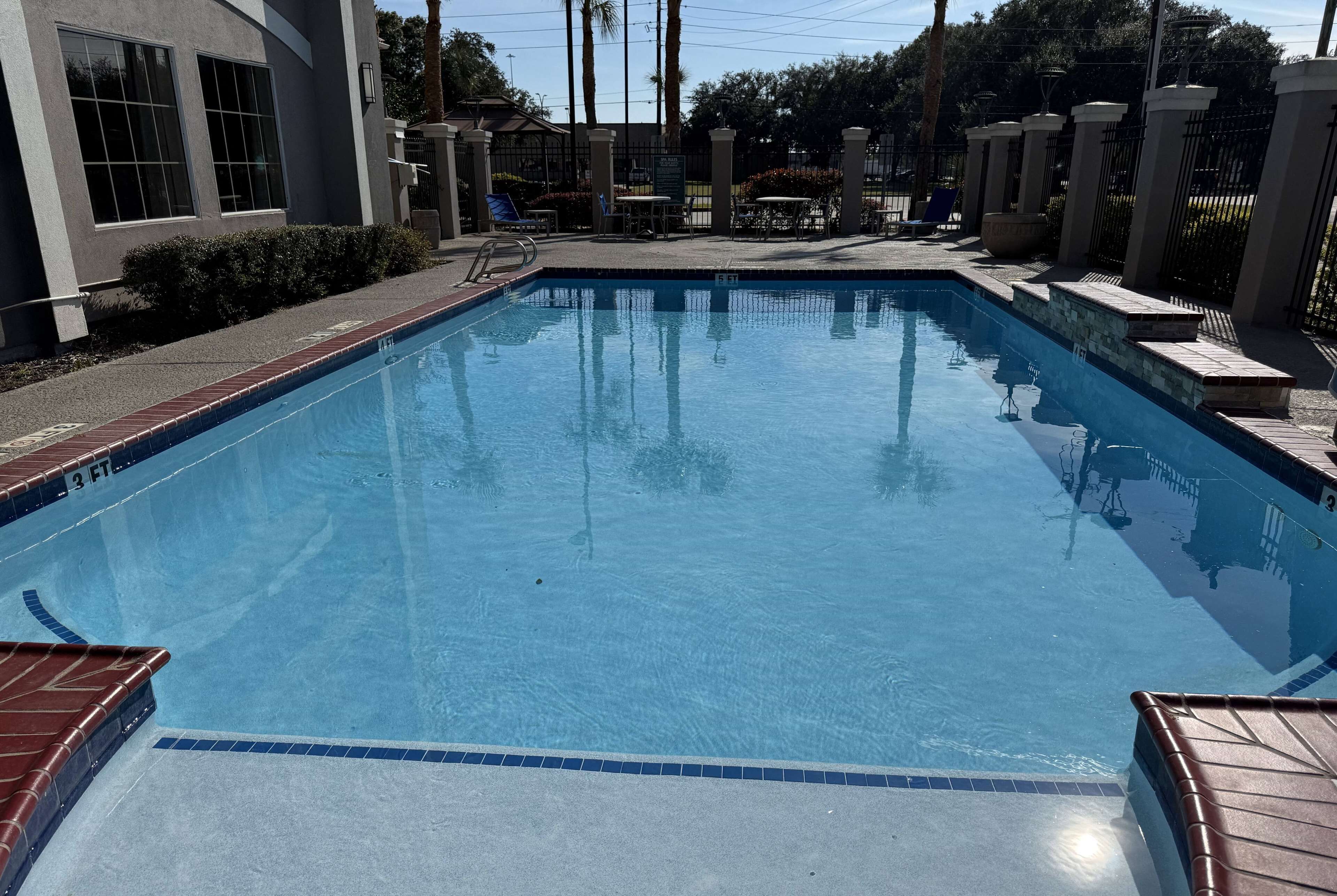 A rectangular swimming pool with a tiled edge, surrounded by a low brick wall and a metal fence.