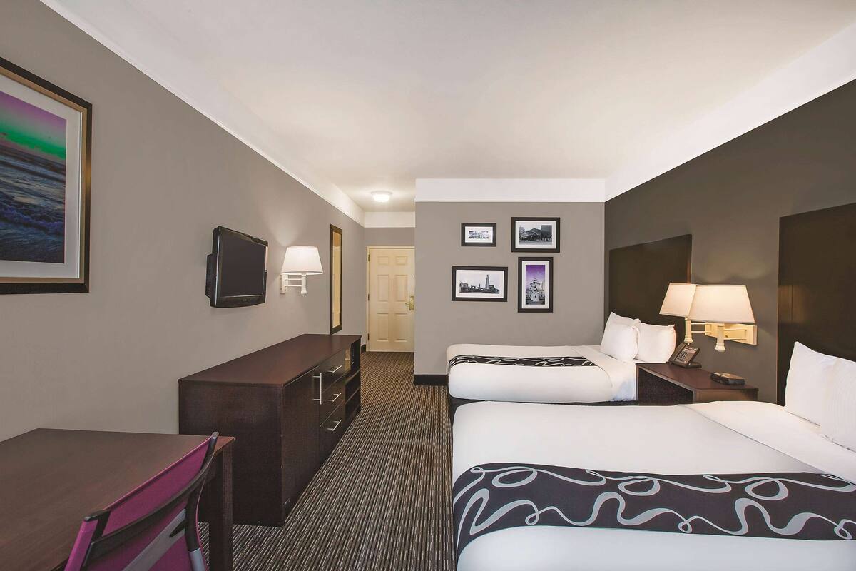 Een hotelkamer met twee bedden, een bureau, een stoel, een televisie en een deur die naar een andere kamer leidt.