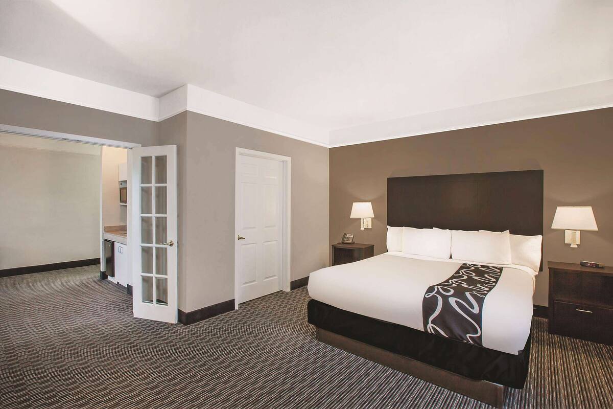 Een hotelkamer met een groot bed, twee nachtkastjes met lampen, een garderobe en een deur naar een inloopkast.
