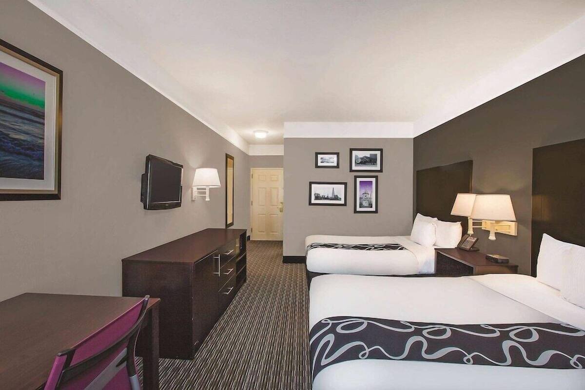 Een hotelkamer met een bureau, twee bedden, een televisie en beelden in lijsten aan de muur.