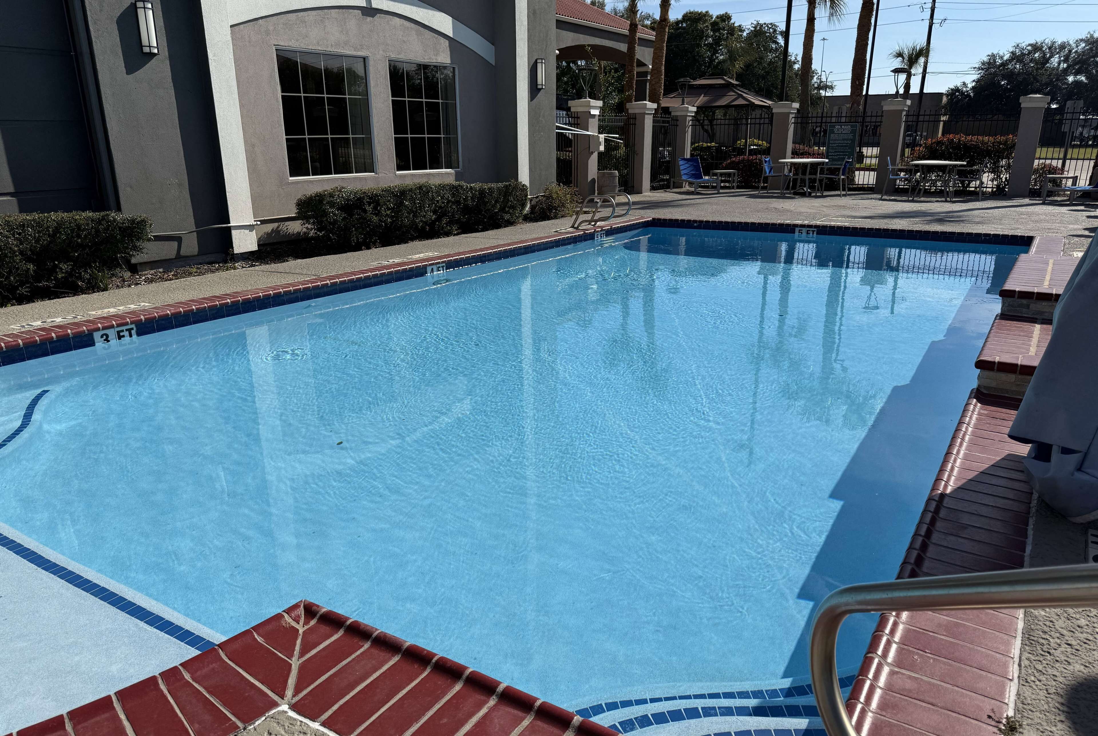 A clear swimming pool with a tiled edge, a brick deck, and a building with large windows in the background.