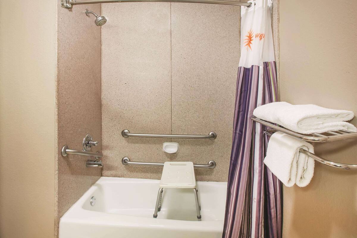 Een badkamer met een bad, douchegordijn, een handgreep, een handdoekhouder en een handdouche.