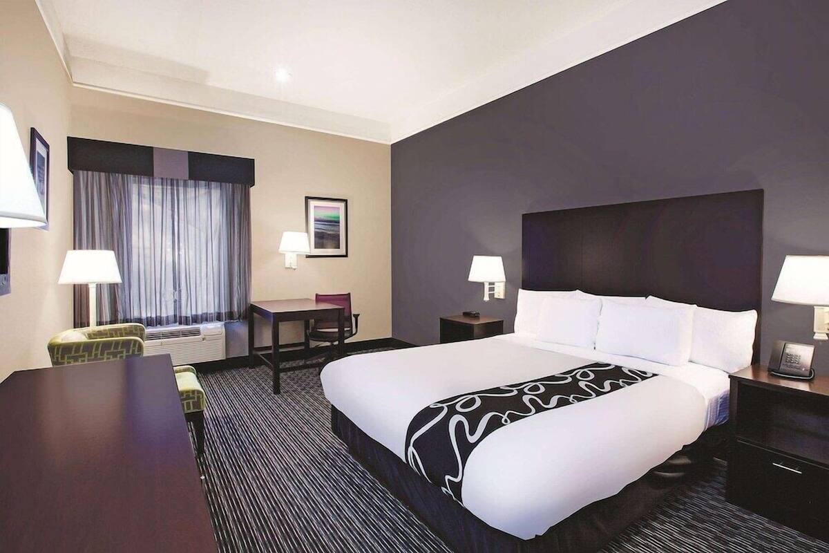 Hotelkamer met een groot bed, een bureau, twee stoelen, een bijzettafeltje, een lamp, een schilderij aan de muur en een raam met gordijnen.
