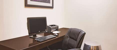 Une chambre d’hôtel équipée d’un bureau, d’un ordinateur, d’une imprimante, d’une chaise et d’un objet métallique posé sur le sol.