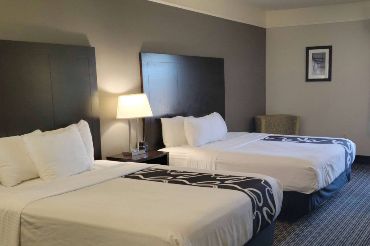Een hotelkamer met twee bedden, een nachtkastje met een lamp, een ingelijst schilderij aan de muur en een stoel.