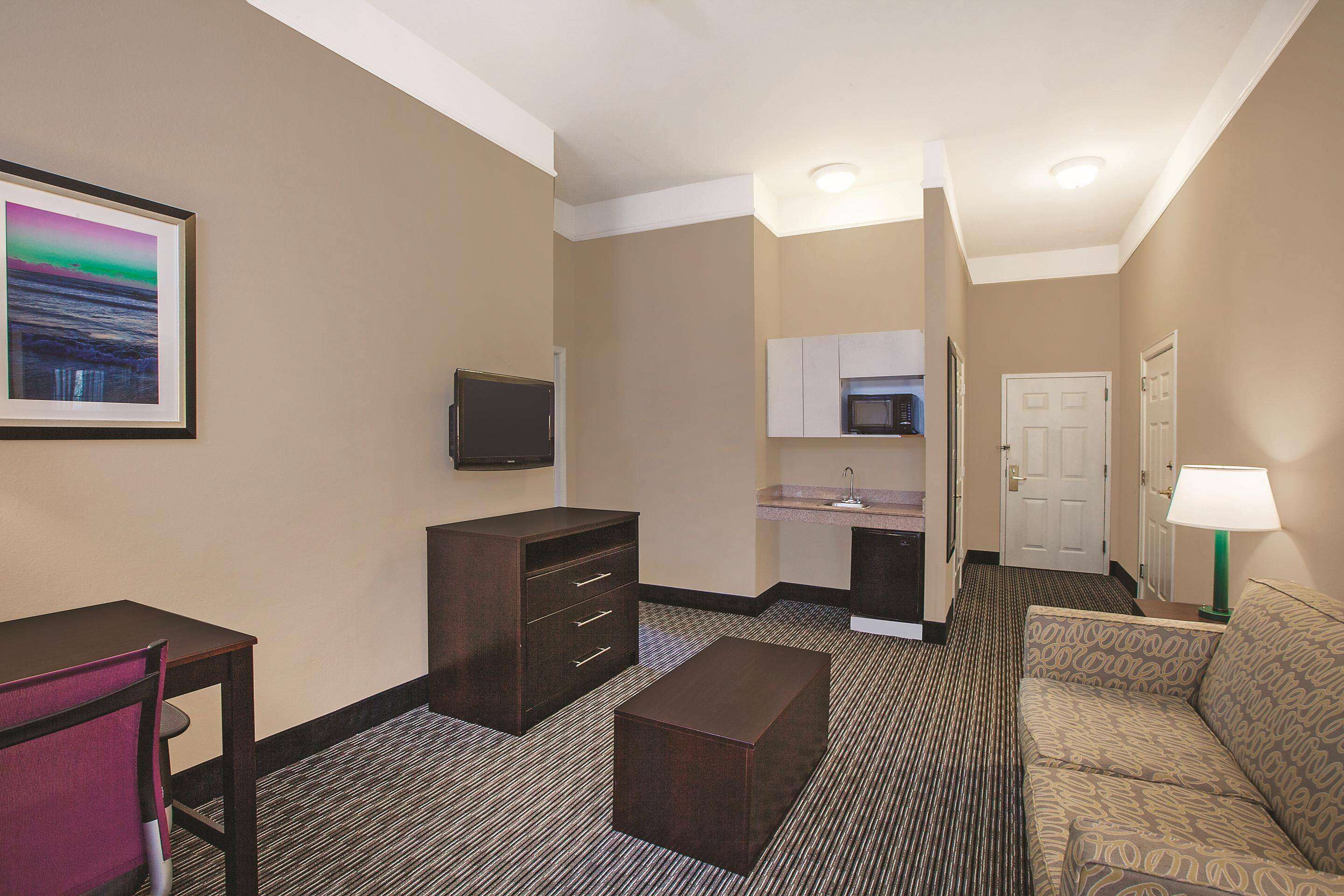 Ein Hotelzimmer mit einer Küchenzeile, einer Couch, einem Schreibtisch, einem Fernseher und einem gerahmten Bild an der Wand.