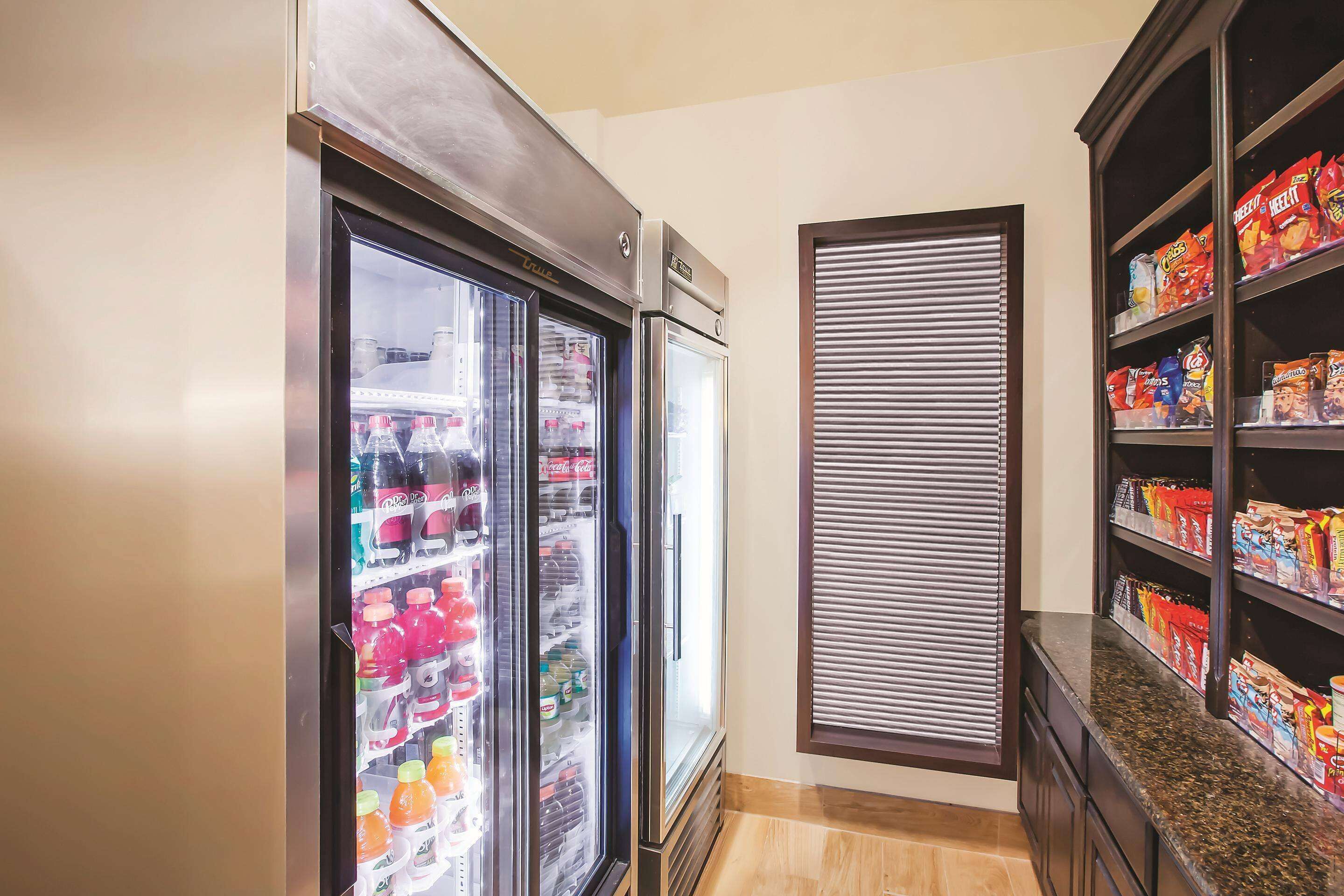 A kitchen with two refrigerators stocked with beverages and a pantry with snacks.