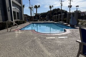 Una piscina con un deck circundante, palmeras y una entrada con puerta de reja.