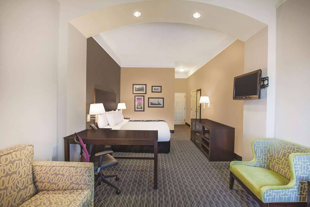 Een hotelkamer met een bed, bureau, twee fauteuils, een televisie en ingelijste foto’s aan de muur.