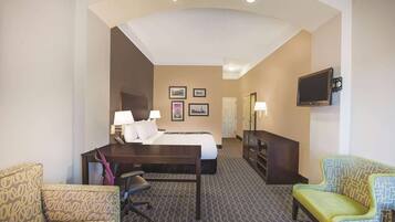 Habitación de hotel con cama, escritorio, dos sillones, televisión y cuadros en la pared.