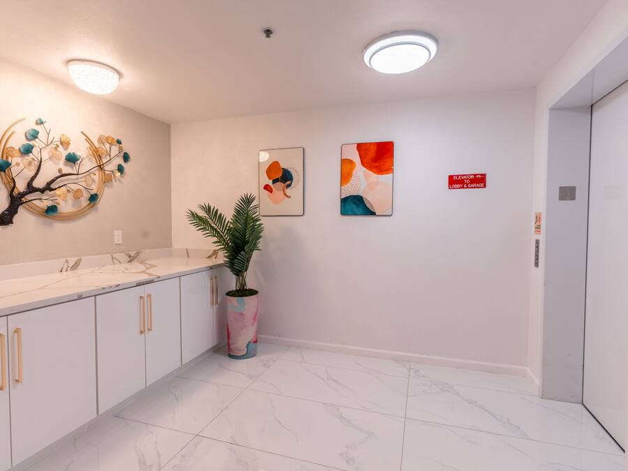 A modern hallway with a marble floor, white walls, and a decorative tree sculpture. There are two framed artworks on the wall and a potted plant.