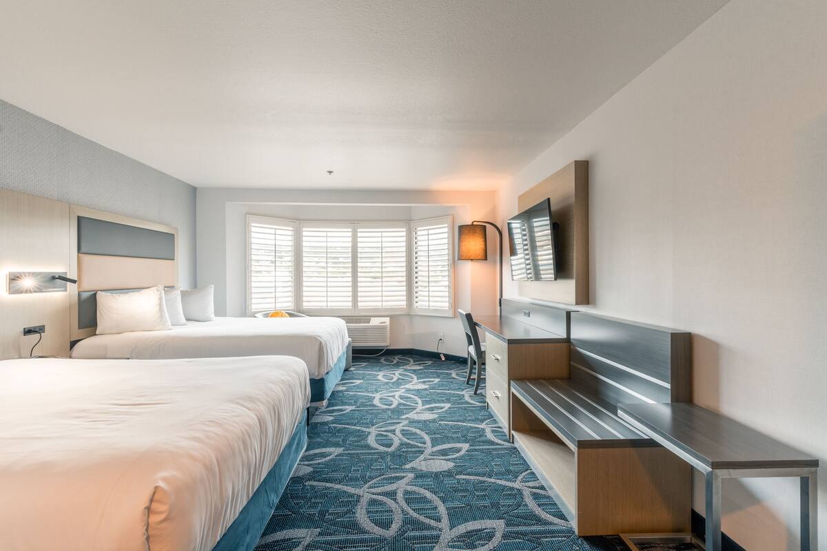 Habitación de hotel con dos camas, un escritorio, un televisor y una ventana con persianas.