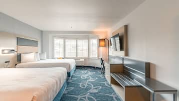 A hotel room with two beds, a desk, a TV, and a window with blinds.