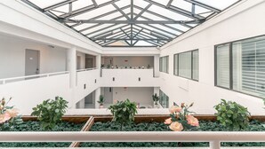 A modern atrium with a glass ceiling, multiple levels, and indoor plants. - Hotel Aluxor SFO (San Bruno)