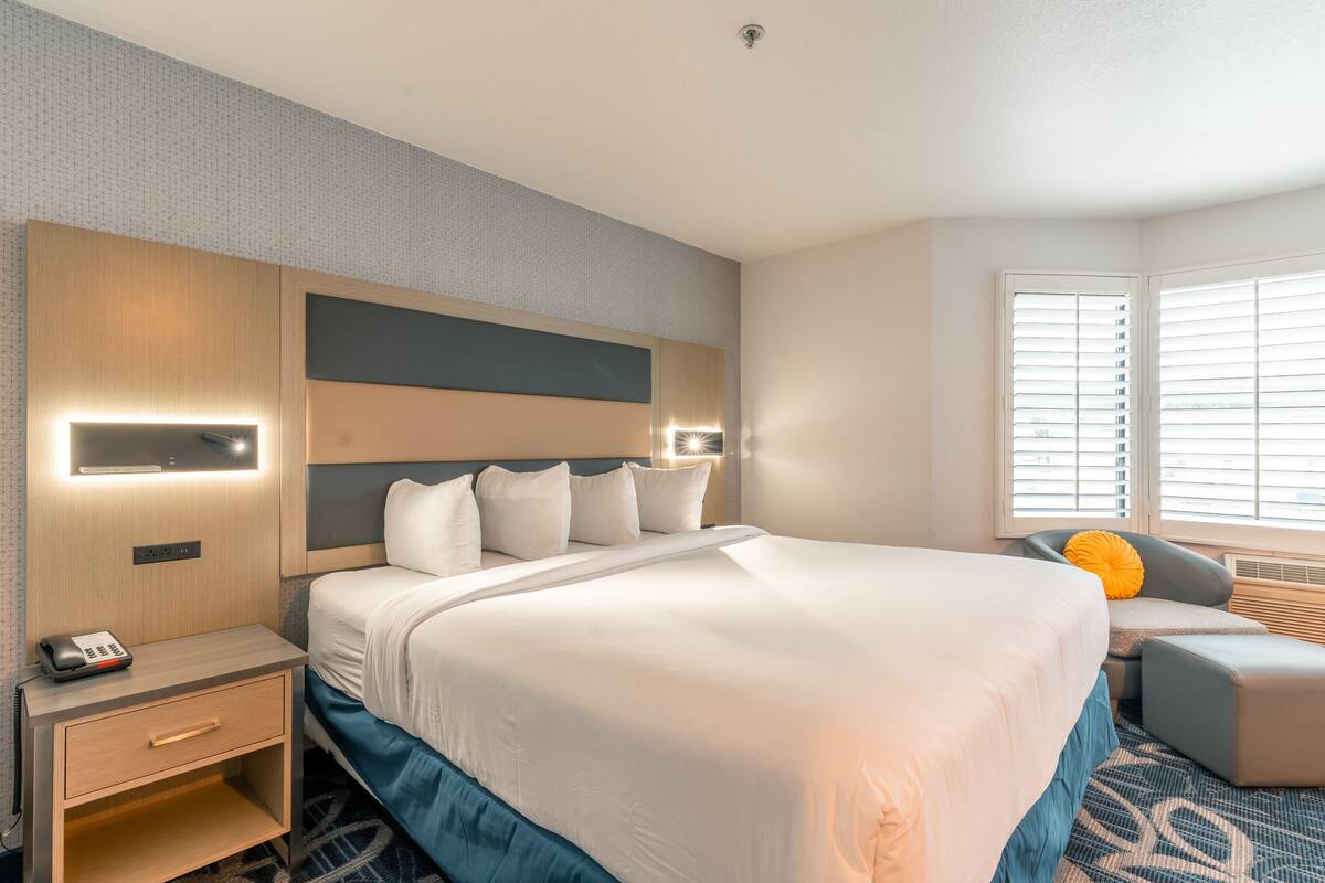 Una habitación de hotel con una cama grande, mesitas de noche, un escritorio y una ventana con persianas.