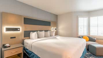 A hotel room with a large bed, bedside tables, a desk, and a window with blinds.