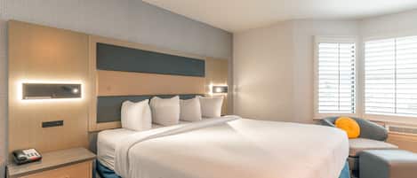 Ein Hotelzimmer mit einem großen Bett, Nachttischen, einem Schreibtisch und einem Fenster mit Jalousien.