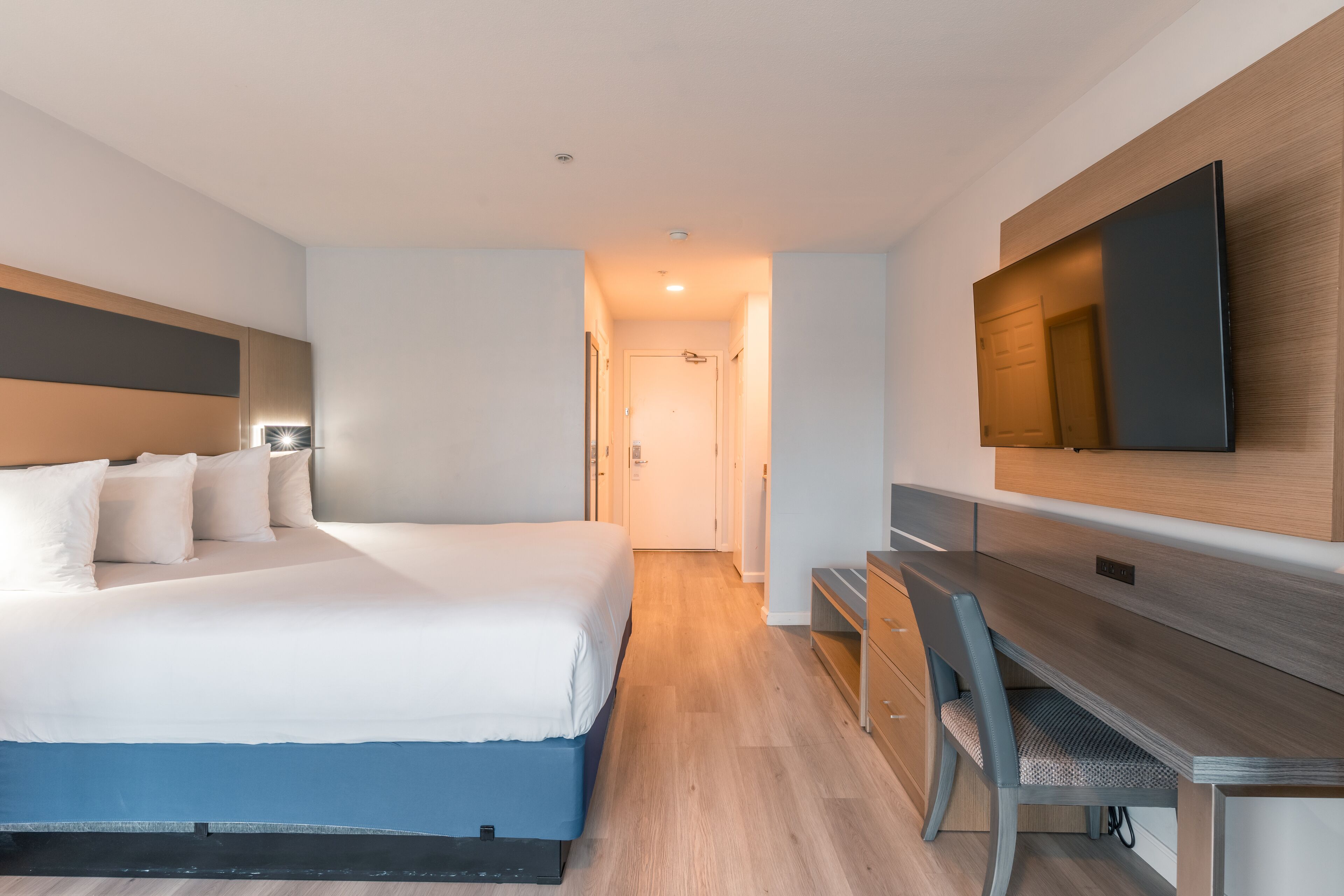 A modern hotel room with a bed, desk, and flat-screen TV.