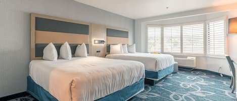A hotel room with two beds, a large window with blinds, a patterned carpet, and a wall-mounted lamp.