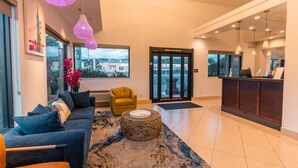 A modern lobby with a sofa, yellow armchair, and a round coffee table. - Hotel Aluxor SFO (San Bruno)