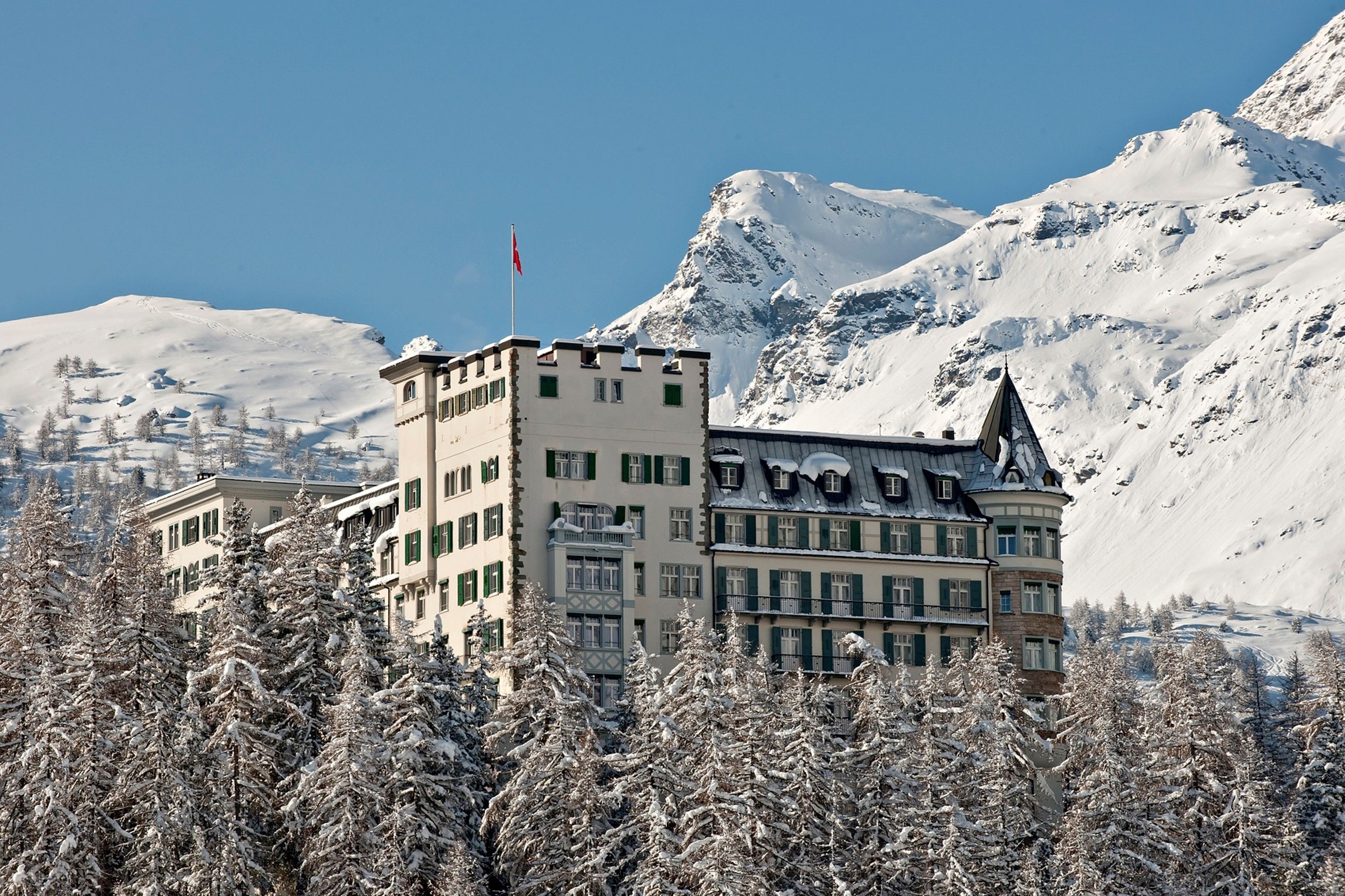 Ett hotell med ett torn och flera byggnader, omgivet av snötäckta träd och berg.