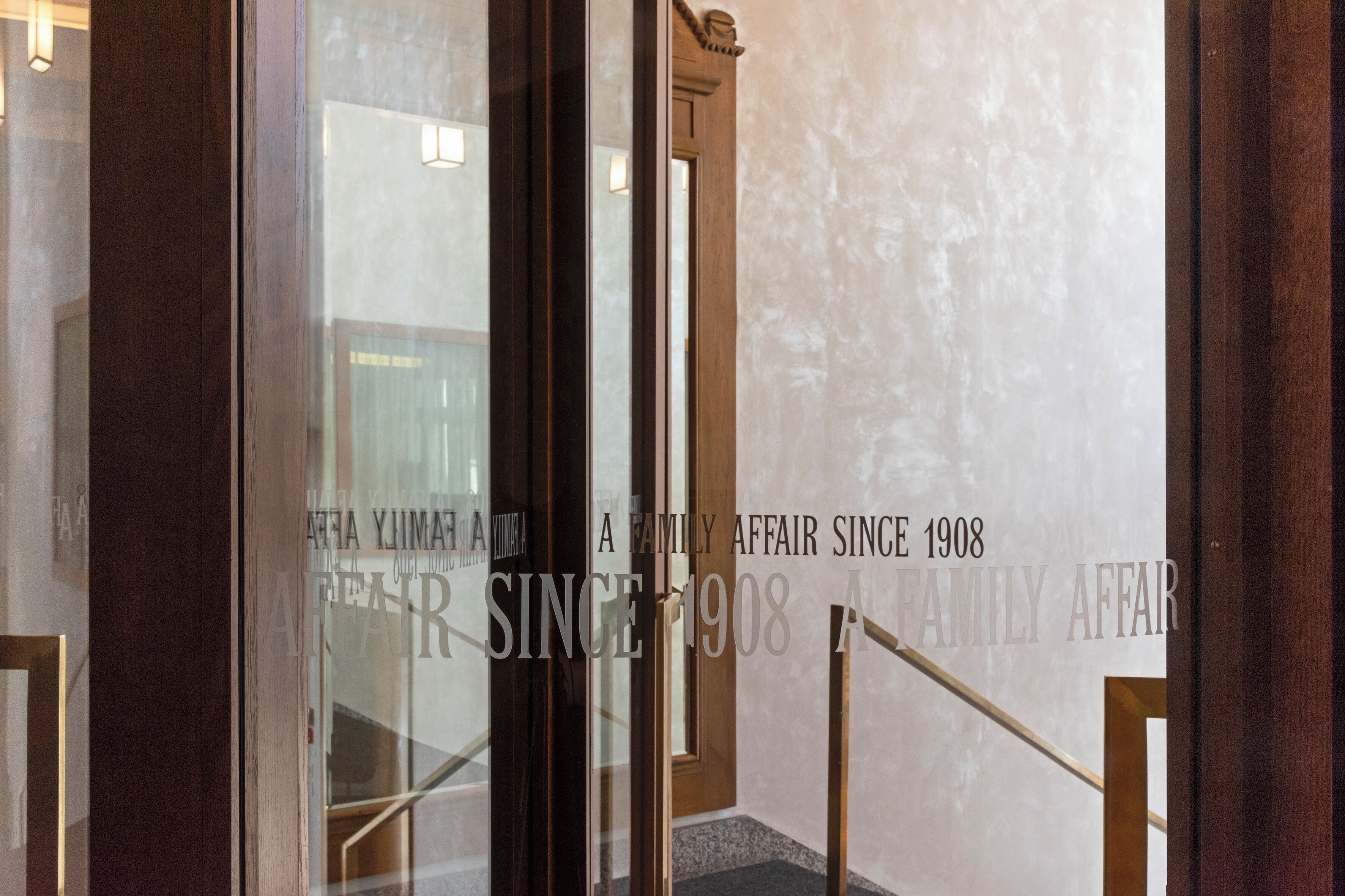 Eine Treppe mit Holzgeländer und einer Glastür, auf der ein Schild mit der Aufschrift "A FAMILY AFFAIR SINCE 1908" steht.