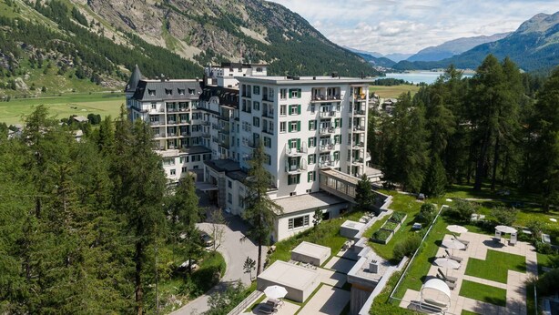 Ein mehrstöckiges Hotel mit Dachpool und Gartenanlage, umgeben von Bergen und einem See.