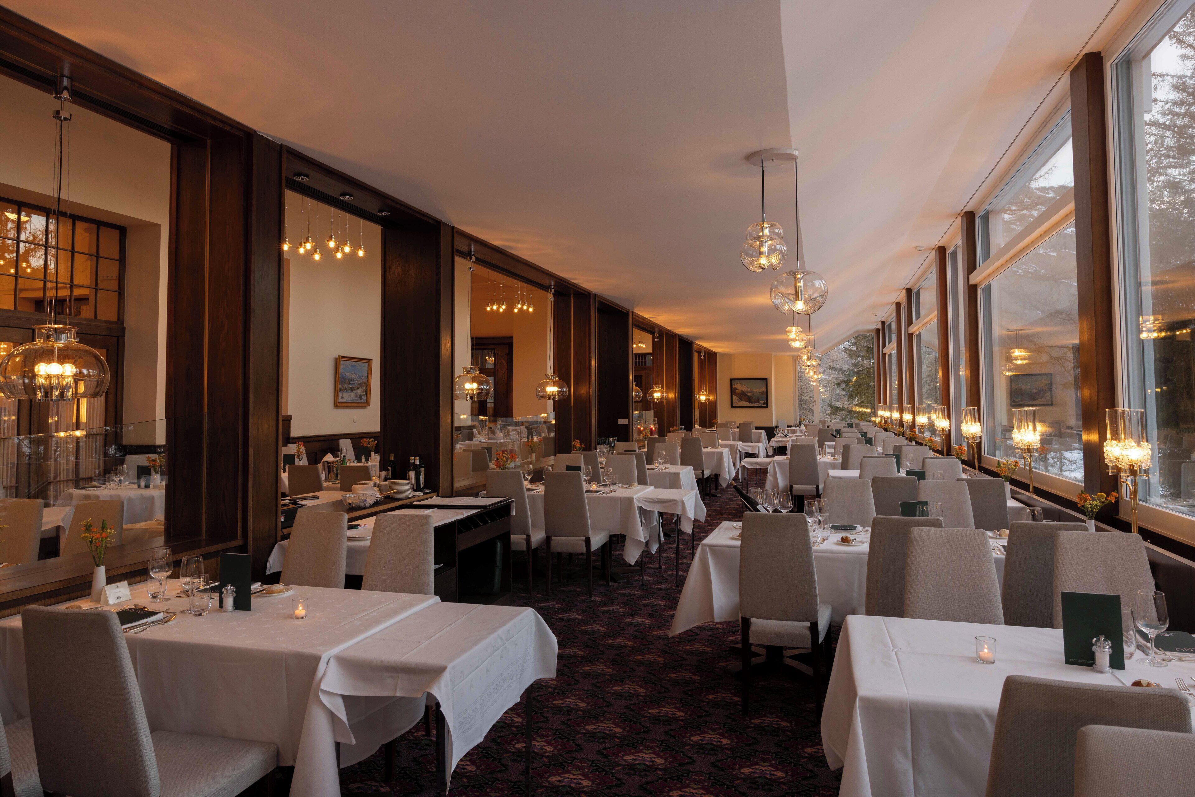 A restaurant with multiple tables, chandeliers, and large windows.