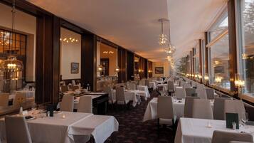 Un restaurant doté de nombreuses tables, de lustres et de grandes fenêtres.