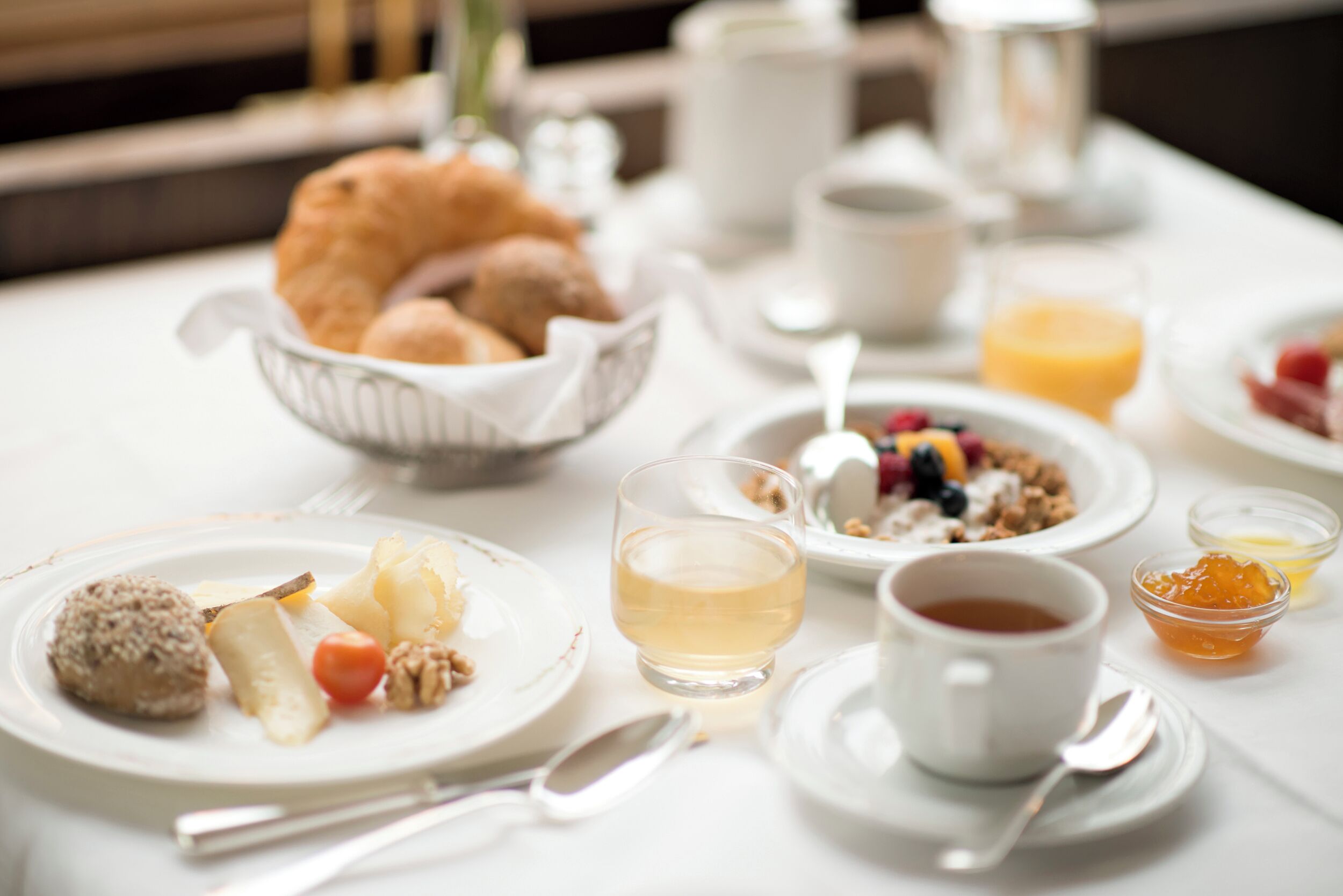 Ein Frühstückstisch mit Tellern voller Speisen, einer Schale Gebäck, einem Glas Saft, einer Tasse Tee und einer kleinen Schale Marmelade.