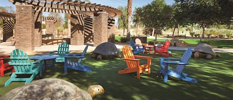 Un patio con mobiliario exterior, incluyendo sillas tipo Adirondack y una estructura de pérgola de madera.