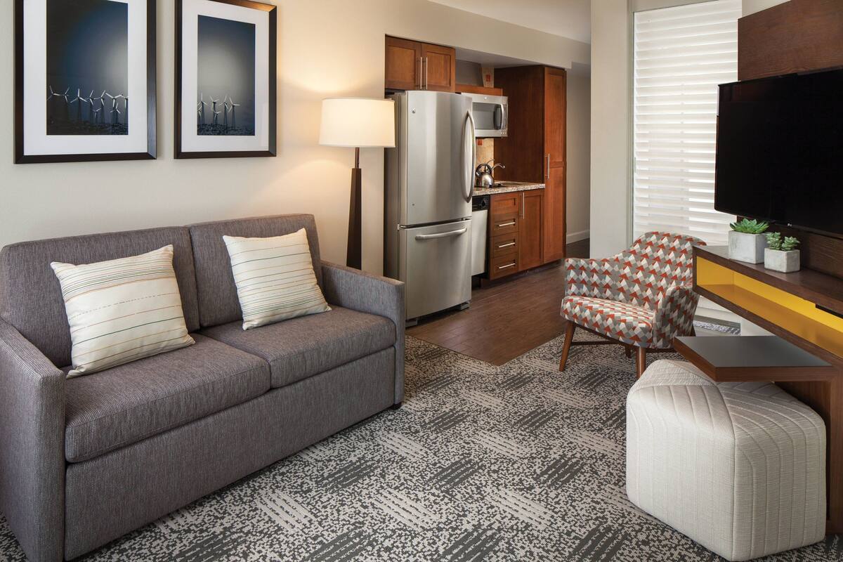 A modern living room with a grey sofa, a patterned armchair, and a flat-screen TV.