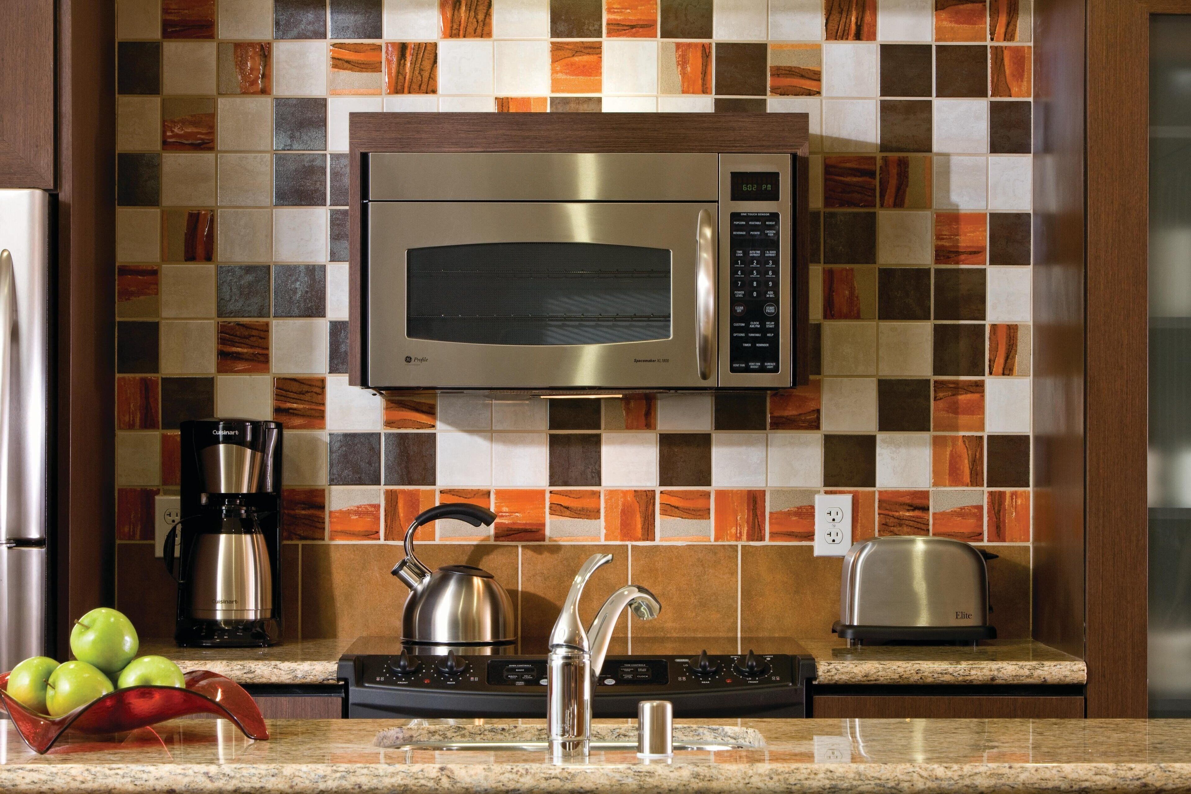 A modern kitchen with a stainless steel microwave, a coffee maker, a kettle, and a toaster on the countertop.