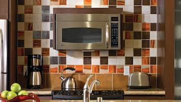 A modern kitchen with a stainless steel microwave, a coffee maker, a kettle, and a toaster on the countertop.
