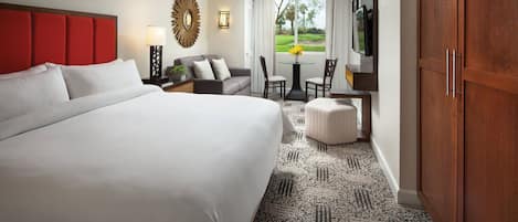 A hotel room with a large bed, a ceiling fan, a seating area with a table and chairs, and a view of a golf course through the window.