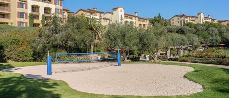 Una cancha de voleibol de arena rodeada de vegetación exuberante y un hotel de varios pisos con balcones al fondo.