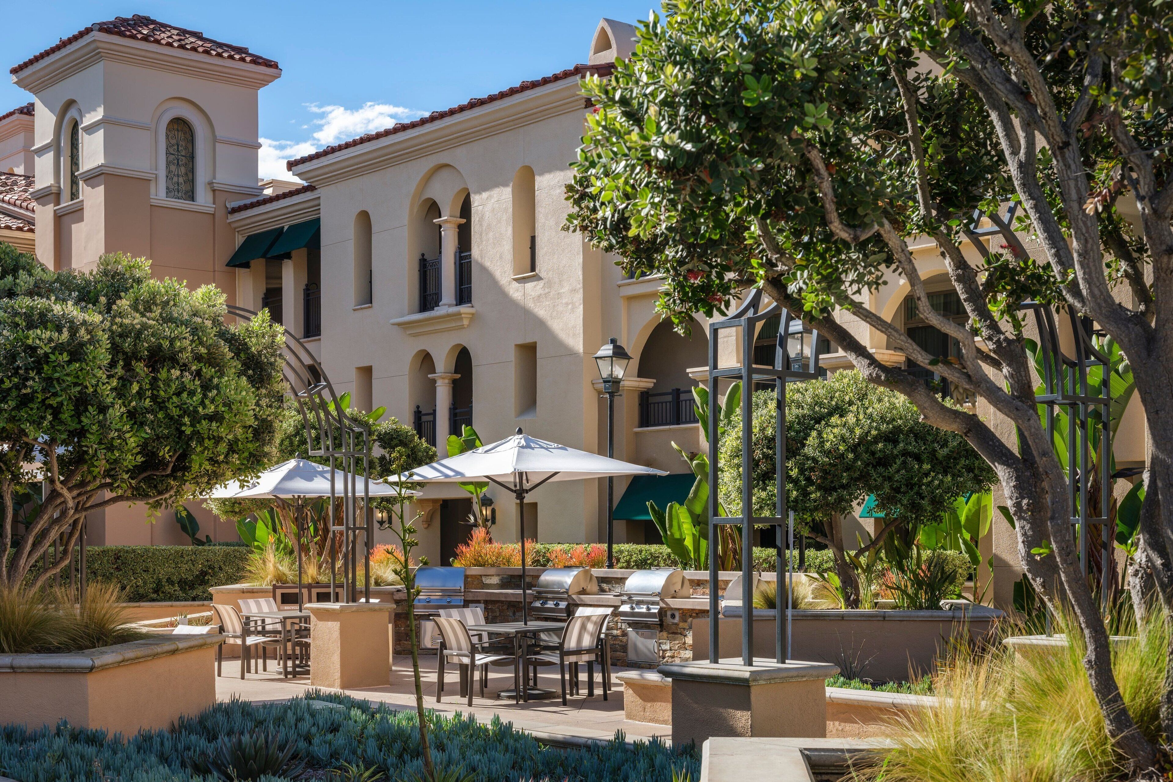 Un patio exterior con una parrilla, asientos y vistas a un edificio con arcos y un tejado de tejas.