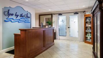 A reception area with a wooden reception desk, a sign reading "Spa by the Sea", and a glass door leading to a room.