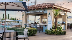 An outdoor bar area with a pool view, bar stools, and umbrellas. - Marriott's Newport Coast Villas (Newport Beach)