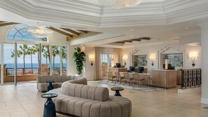 A spacious living area with a curved sofa, two side tables, a dining area with chairs, a kitchen counter, and large windows offering a view of palm trees and the ocean. - Marriott's Newport Coast Villas (Newport Beach)