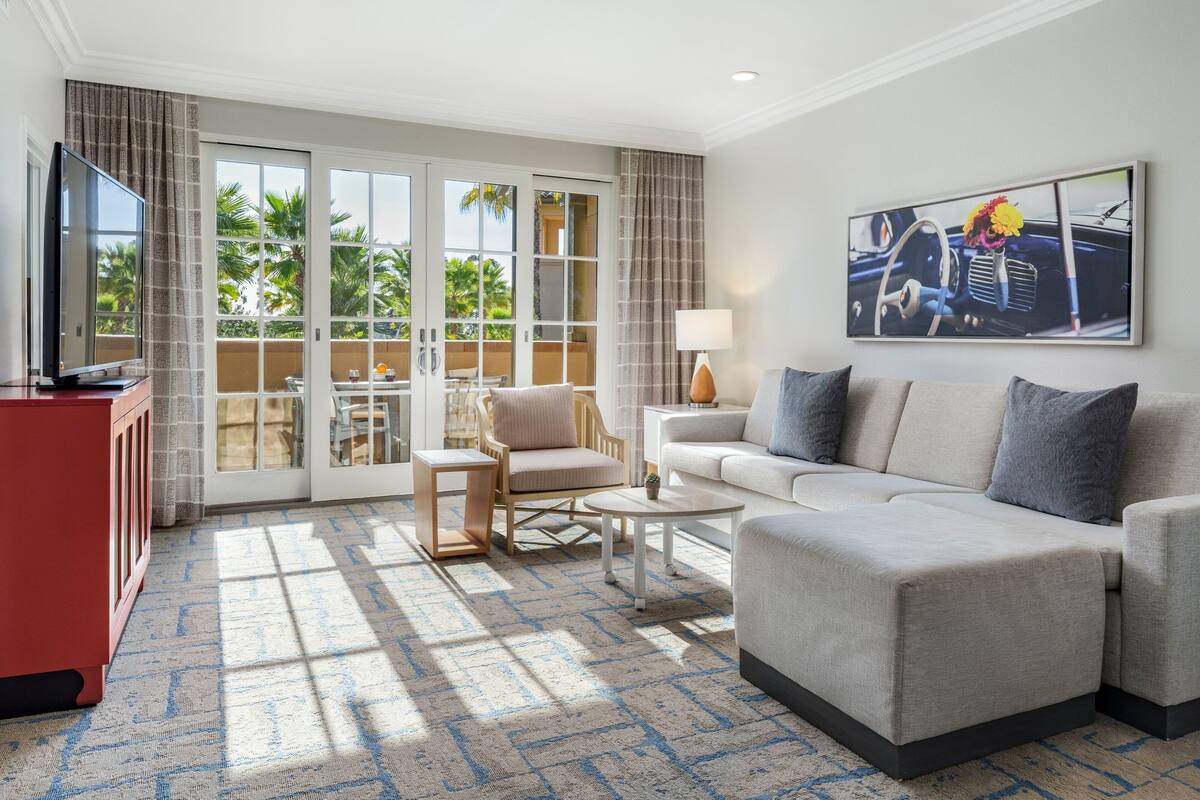 A modern living room with a sofa, armchair, and coffee table. There is a television on a stand and a painting on the wall.