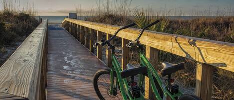 Un muelle de madera que conduce a la playa, con una bicicleta verde estacionada allí.