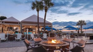 An outdoor seating area with wicker chairs and a fire pit, overlooking a beach. - Marriott's Grande Ocean (Hilton Head Island)